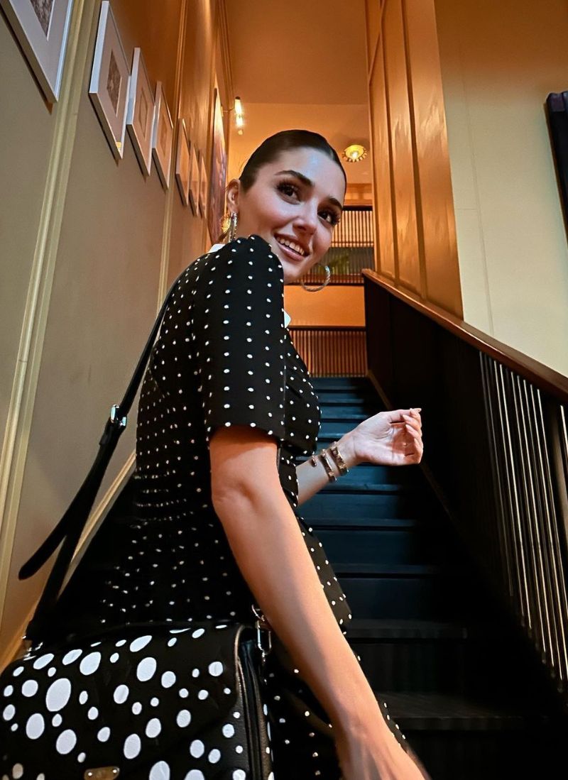 Hande Erçel subiendo unas escaleras con un vestido negro de lunares blancos