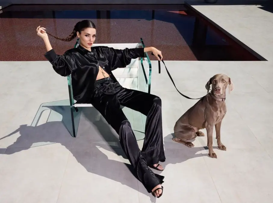 Posado de Hande Erçel con trenza y un perro sentada junto a una piscina
